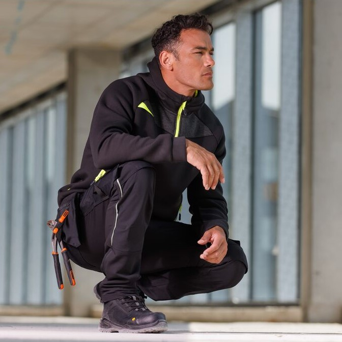 Worker in black protective clothing kneeling on the floor in a warehouse.