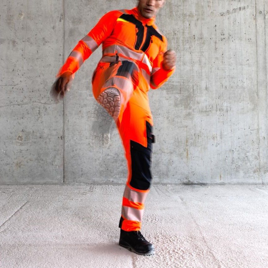 Worker in orange protective clothing lifting one leg in a kicking motion.