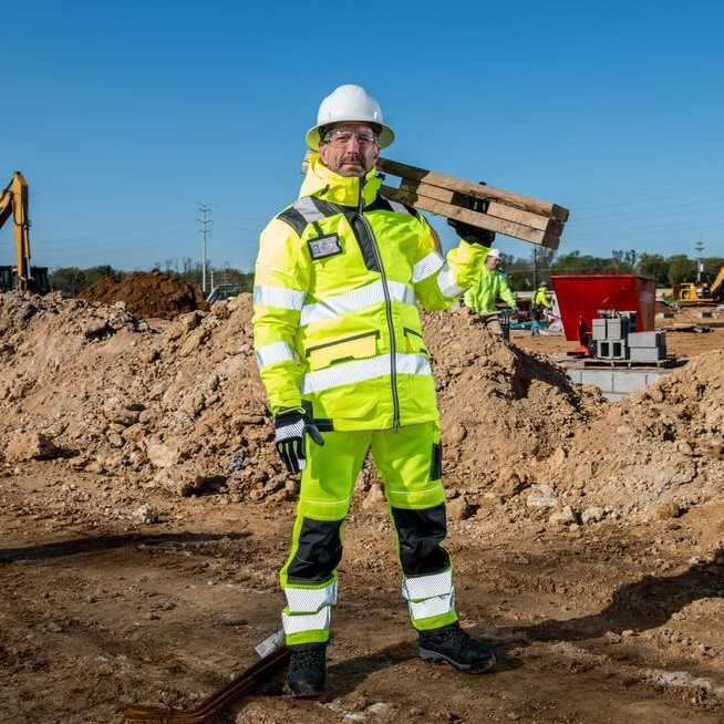 Man in high-visibility yellow workwear standing on a construction site under a blue sky.