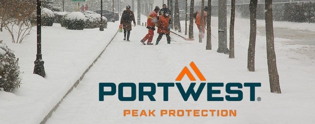 Snow-covered sidewalk with heavily bundled pedestrians, trees and people in high-visibility clothing shoveling snow.