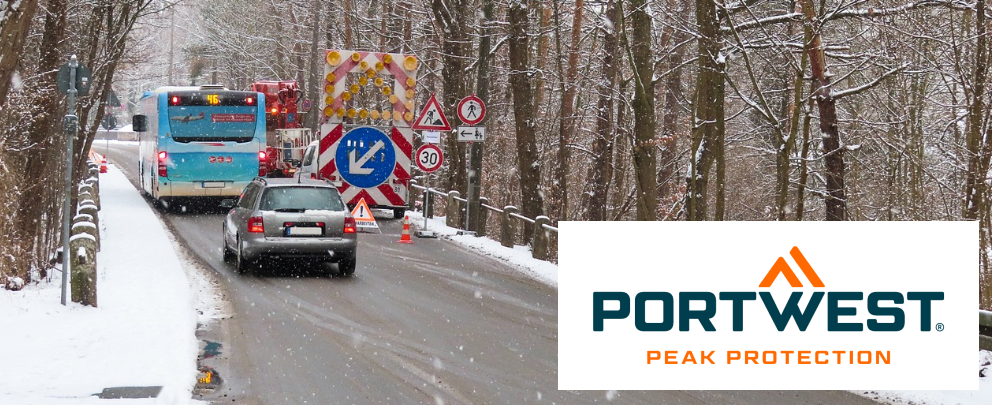 Construction site scene with bus and car on a snowy road surrounded by trees. In the right corner there is the Portwest brand logo.