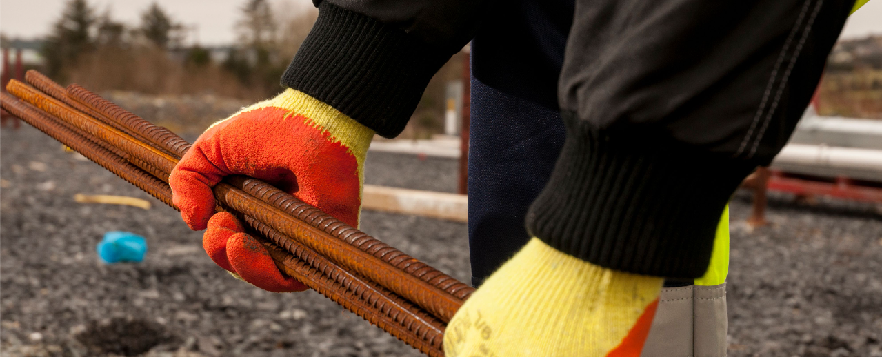 Model image of the Fortis Grip A150 glove in yellow/orange working with rebar.