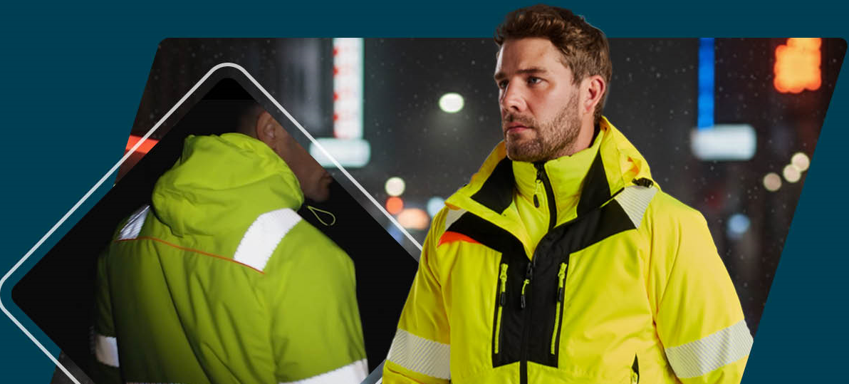 A worker in yellow high-visibility clothing with reflective stripes and black details. In the background, a dark street with blurred lighting is visible. The back of the jacket is shown on the left.