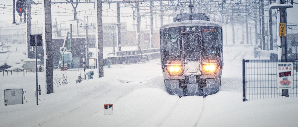 Front view of a train. The tracks are covered in snow, and visibility is poor due to the falling snow.