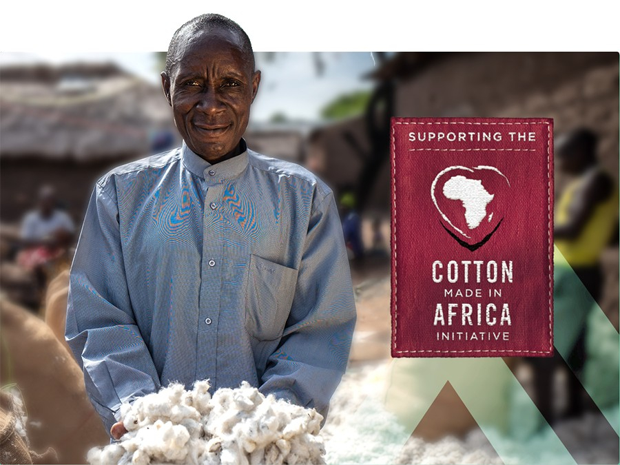 African farmer wearing a blue shirt and presenting a handful of cotton. A deep red sign reading "Supporting the Cotton Made In Africa Initiative" is in the right half of the image.