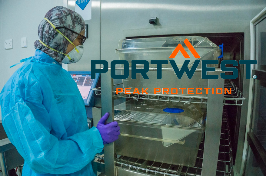 Person in blue disposable lab clothing in front of a stainless steel cabinet. The Portwest manufacturer logo in orange and blue is visible on the right. A link to our lab clothing is included.