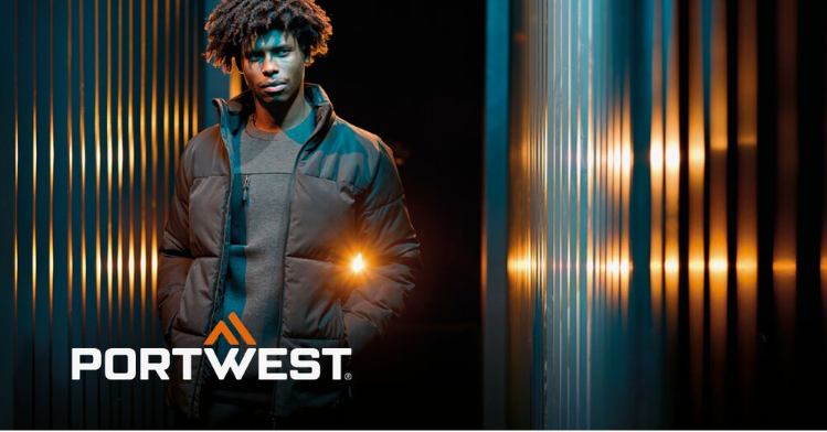 A worker in black workwear against an abstract background with a striped wall and light reflections. The manufacturer's logo, Portwest, in white and orange, is located in the lower left corner of the image.