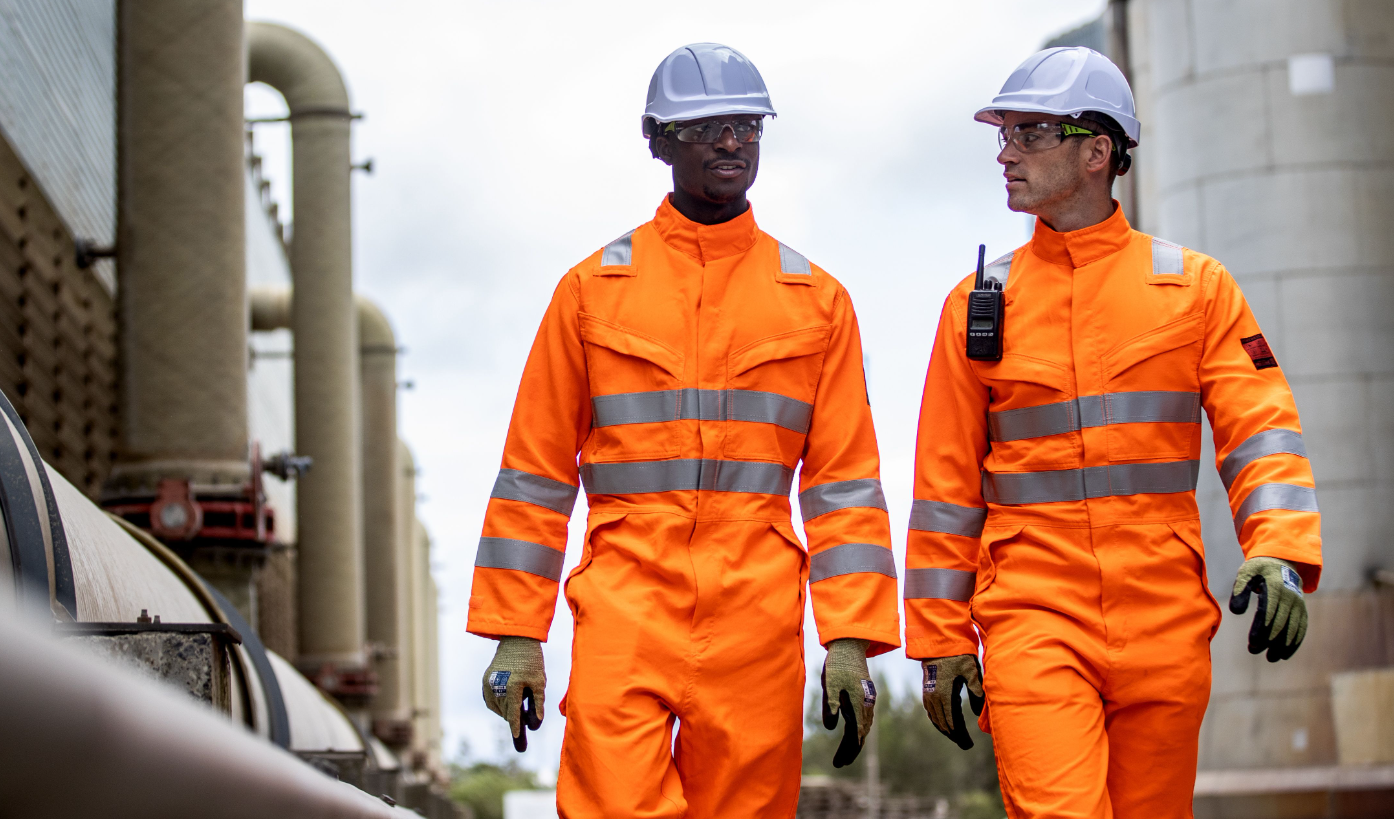 Two workers in front of industrial background wearing orange high visibility clothing and white hard hats. A link to the Endurance Glowtex helmet PG54 is available.