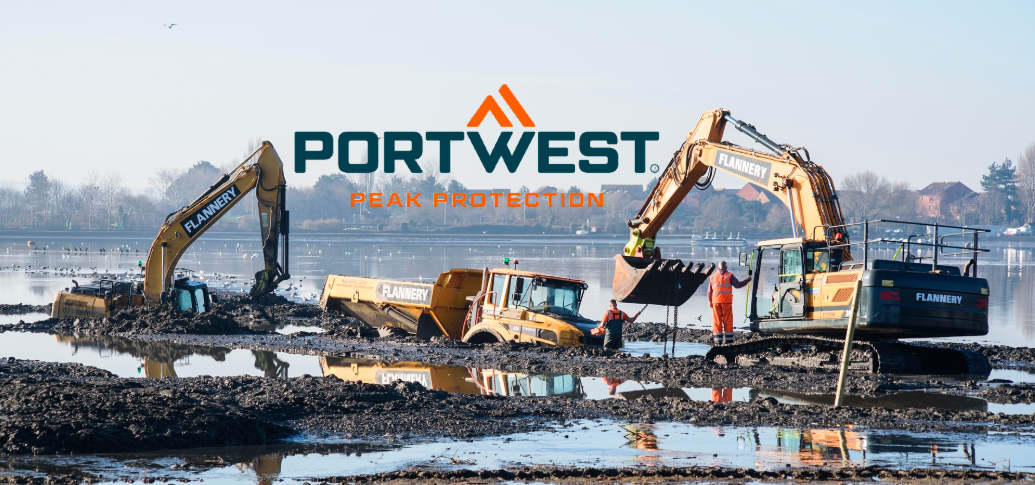 A construction site scene shows two yellow excavators and other vehicles standing in a large mud puddle. In the background, a faint row of houses and trees can be seen under a light blue sky. The blue and orange logo of the manufacturer Portwest is positioned between the crane arms.